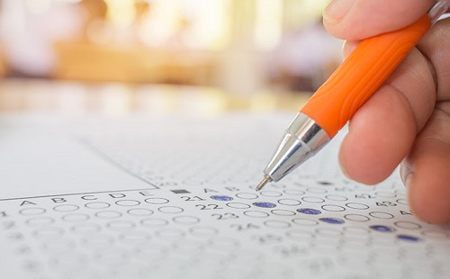 Students hand testing doing examination with pen drawing selected choice on answer sheets in school exams, blur pupils college backgroud. Education system tests concept.